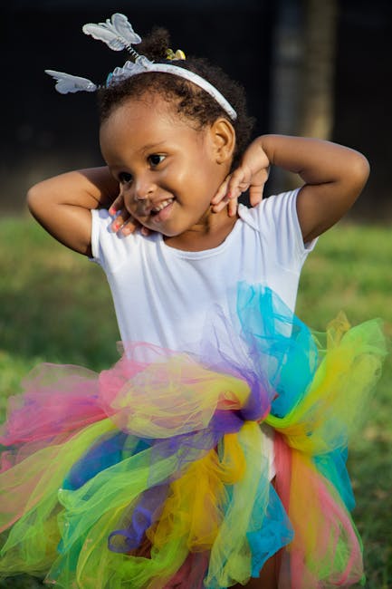 Charming young girl in a vibrant tutu smiling in a sunny outdoor setting.